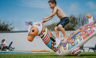 A young white boy, jumping onto an inflatable lama into the outside pool. image