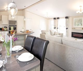 The interior of one of our Luxury holiday lodges. There's a dining area, kitchen section, and two grey sofas.