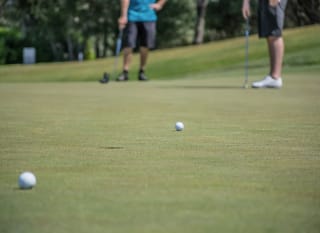 A close up image of two tennis balls at Playgolf Colchester. There are two people standing in the background. image