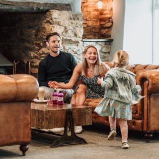 A little girl running towards her mum and dad, who are sat on the sofa in one of our on park restaurants. image