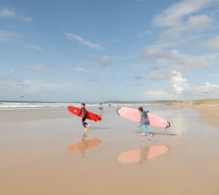 Two children running on the beach with surf boards towards the sea. image