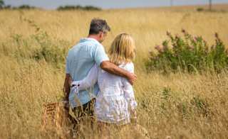 A couple walking in a tall grass field, arm in arm, carrying a wicker picnic basket. image