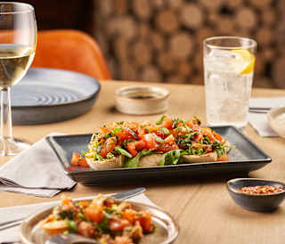 A slate grey rectangle plate with toasted ciabatta, chopped tomato, basil and olive oil. Some of the many tasty items on the menus at our holiday parks.