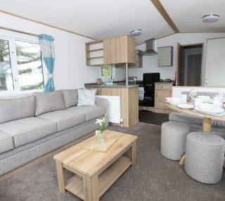 Suggested: The interior of one of our luxury caravans. There's a large, grey sofa, a seating area with a table, and a kitchen space with several appliances. image