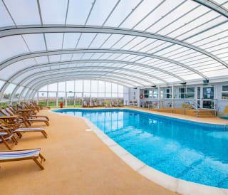 A view of the indoor swimming pool at our Essex holiday park, Mersea Island. Multicoloured deck chairs can be seen around the pool.