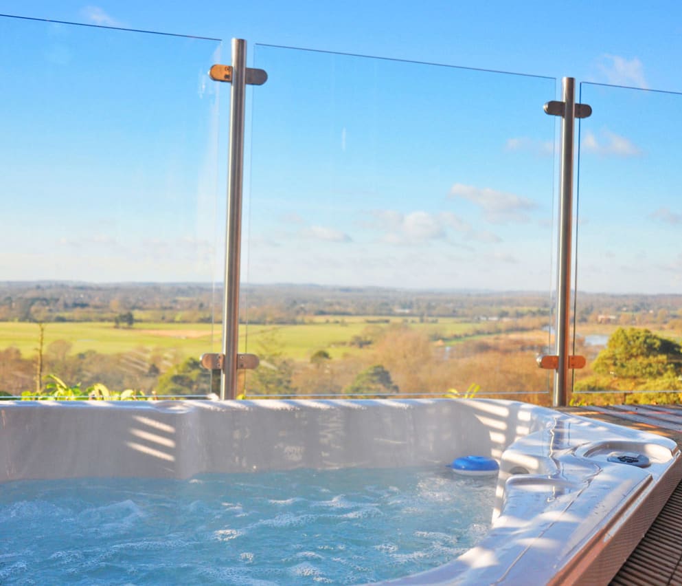A closeup photo of an outdoor hot tub next to glass fencing on a bright sunny day at out holiday park in Sandy Balls, Hampshire.