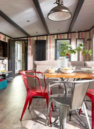 An image of the interior of one of our holiday lodges. There's wooden panneling, a cream fabric sofa and red metal dining chairs around a wooden table.
