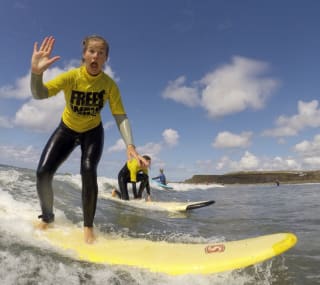 A girl surfing in the sea whilst waving at the camera. image