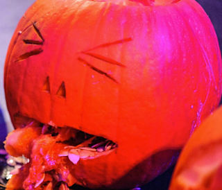 A carved pumpkin with pulp and seeds coming out its mouth to look like gruesome sick.
