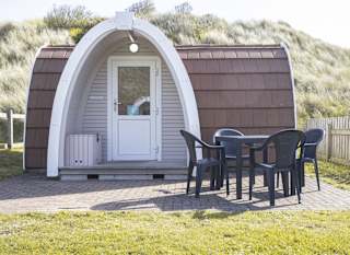 Exterior of our camping pod at St Ives Bay, Cornwall. A table and chair is located on the right, the perfect spot for brunch in the sunshine. image
