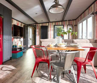 An image of the interior of one of our holiday lodges. There's wooden panneling, a cream fabric sofa and red metal dining chairs around a wooden table.