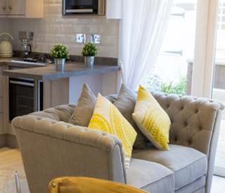 One of our luxury cottage lounges. There's a dining area with a large grey sofa and kitchen. The large double windows are letting the sunlight shine through to brighten the room.