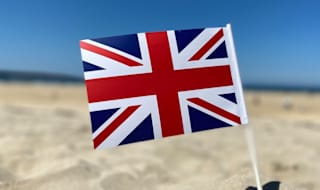 A union jack flag in the sand on a sunny day.