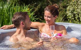 A white couple sitting in a bubbling hot tub outside on a sunny day. image