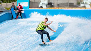 A young male is surfing on a wave stimulator with two other males watching from the sideline.