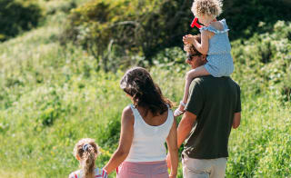 Back shot of family of four walking together, young girl on dad's shoulders and other young girl holding mother's hands. image