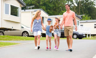 A family holding hands walking through one of our stunning holiday pars. There is a row of caravans in the background. image