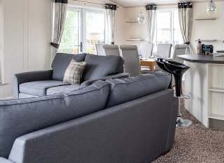 The interior of one of our Indulgent holiday lodges. There are two grey sofas and a spacious dining area. image