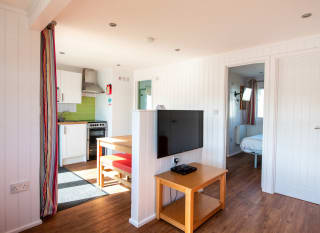 The interior of one of our holiday home Chalets. There’s a large TV, double bedroom, and kitchen space. There are bright colours in the holiday home. image
