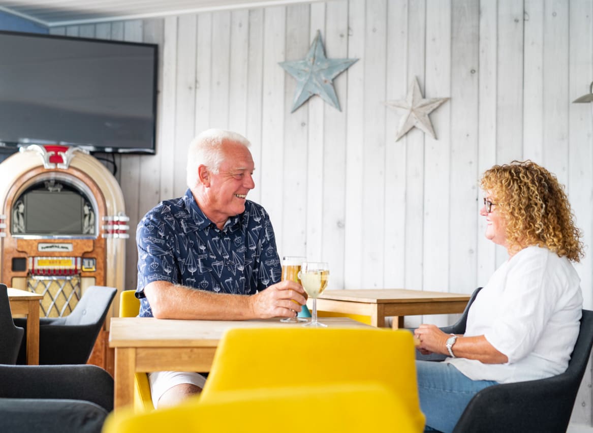 A couple enjoying a drink together at The Muddy Duck Clubhouse at our Essex holiday park, Mersea Island. image