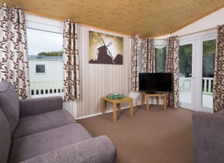 The interior of one of our Superior lodges. There are two grey sofas, a TV, and double-doors leading outside. image