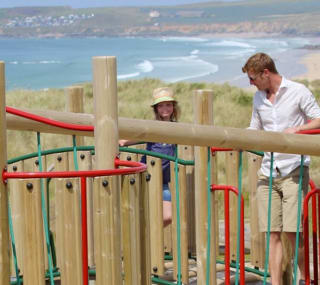 A father and son playing in the outdoor playground at our St Ives Bay Holiday Park with views of the sea in the background. image