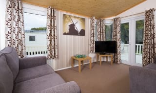 The interior of one of our Superior lodges. There are two grey sofas, a TV, and double-doors leading outside. image