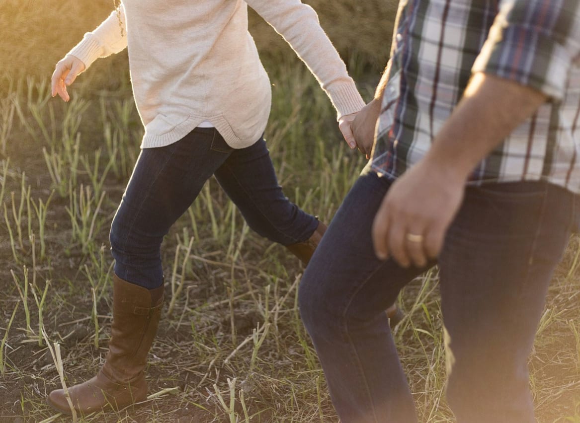 A close up image of two people holding hands on a walk through some taller grass. image