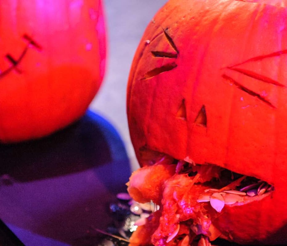 A carved pumpkin with pulp and seeds coming out its mouth to look like gruesome sick.