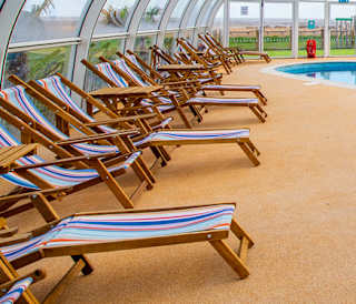 A view of the indoor swimming pool at our Essex holiday park, Mersea Island. Multicoloured deck chairs can be seen around the pool.