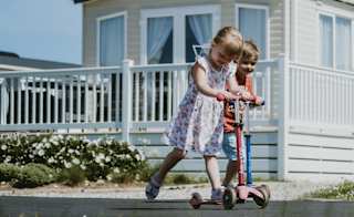 A child riding on their scooter outside one of our stunning holiday homes at Newperran Holiday Resort, Cornwall, on a summers day. image