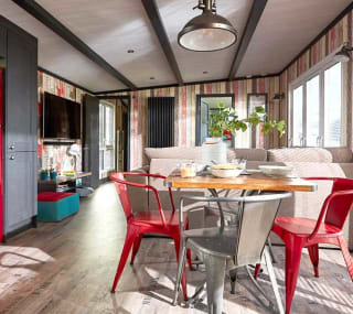 An image of the interior of one of our holiday lodges. There's wooden panneling, a cream fabric sofa and red metal dining chairs around a wooden table. image