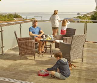 A family of four on the balcony of their holiday home in The Bay Colwell. There are two adults, a young boy, and a young girl with strawberry blonde hair, and all dressed in summer attire.