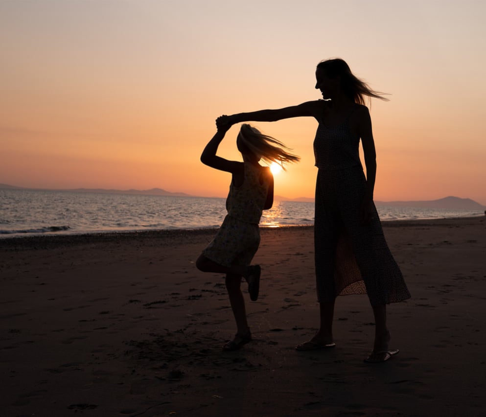 A mother and daughter dancing on the beach at sunset.
