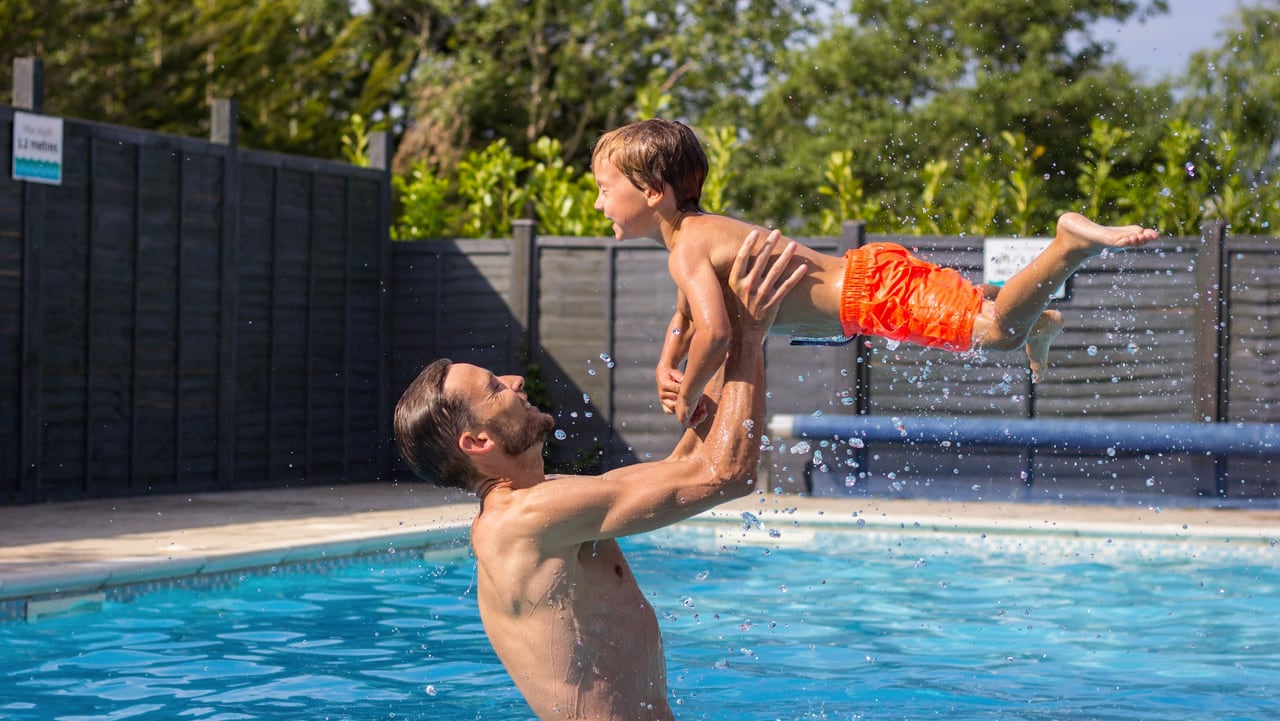 A father and son enjoying a splash in the heated outdoor pool at our stunning resort on the Isle of Wight, The Lakes Rookley.