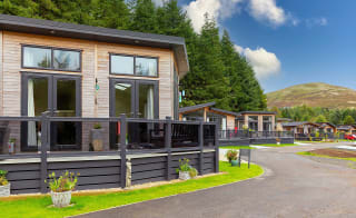 A view of the exterior of our stunning holiday homes for sale at Glendevon Residential Country Park, Scotland. There is a row of wooden lodges and views in the background of the stunning surrounding scenery. image