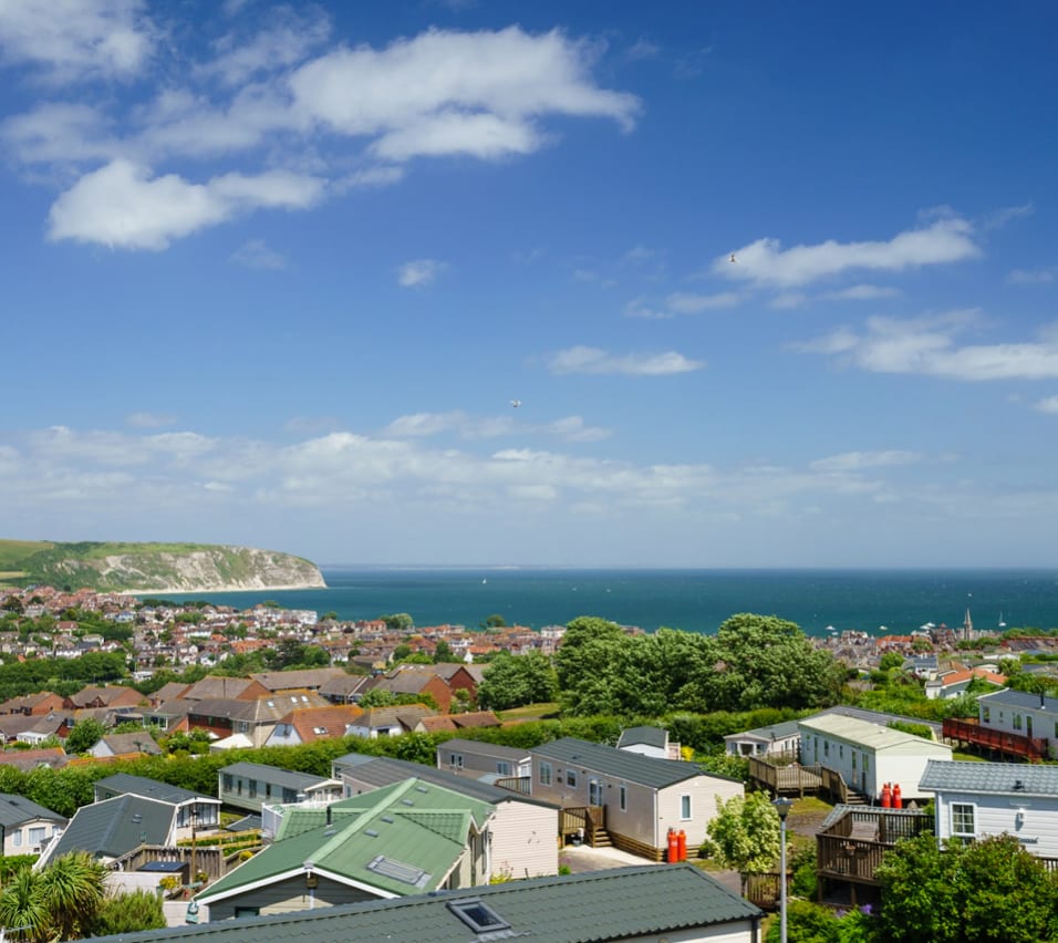 One of our holiday parks in Swanage bay. The bright, sunny day is showing the many holiday homes in the park, along with a view of Dorset, the sea, and the cliffs. image