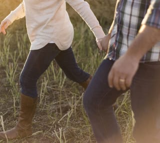 A close up image of two people holding hands on a walk through some taller grass. image