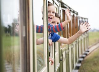 Two children waving at the camera out the window of a train. image