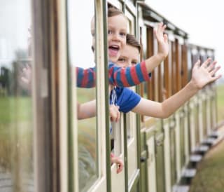 Two children waving at the camera out the window of a train.