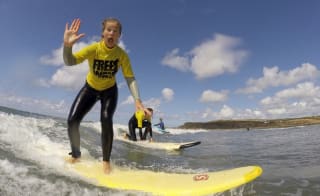 A girl surfing in the sea whilst waving at the camera. image