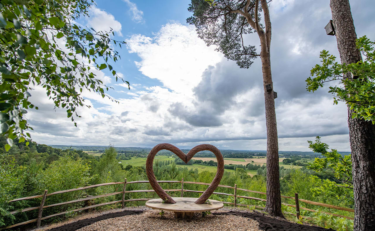 A panoramic view of the countryside, with a viewing area in the foreground. The bench features a wooden heart arch. image