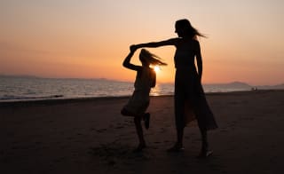 A mother and daughter dancing on the beach at sunset. image