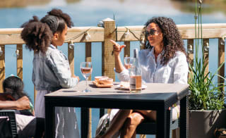 Mother and young daughter sitting lakeside enjoying lunch and drinks together in the sunshine. image