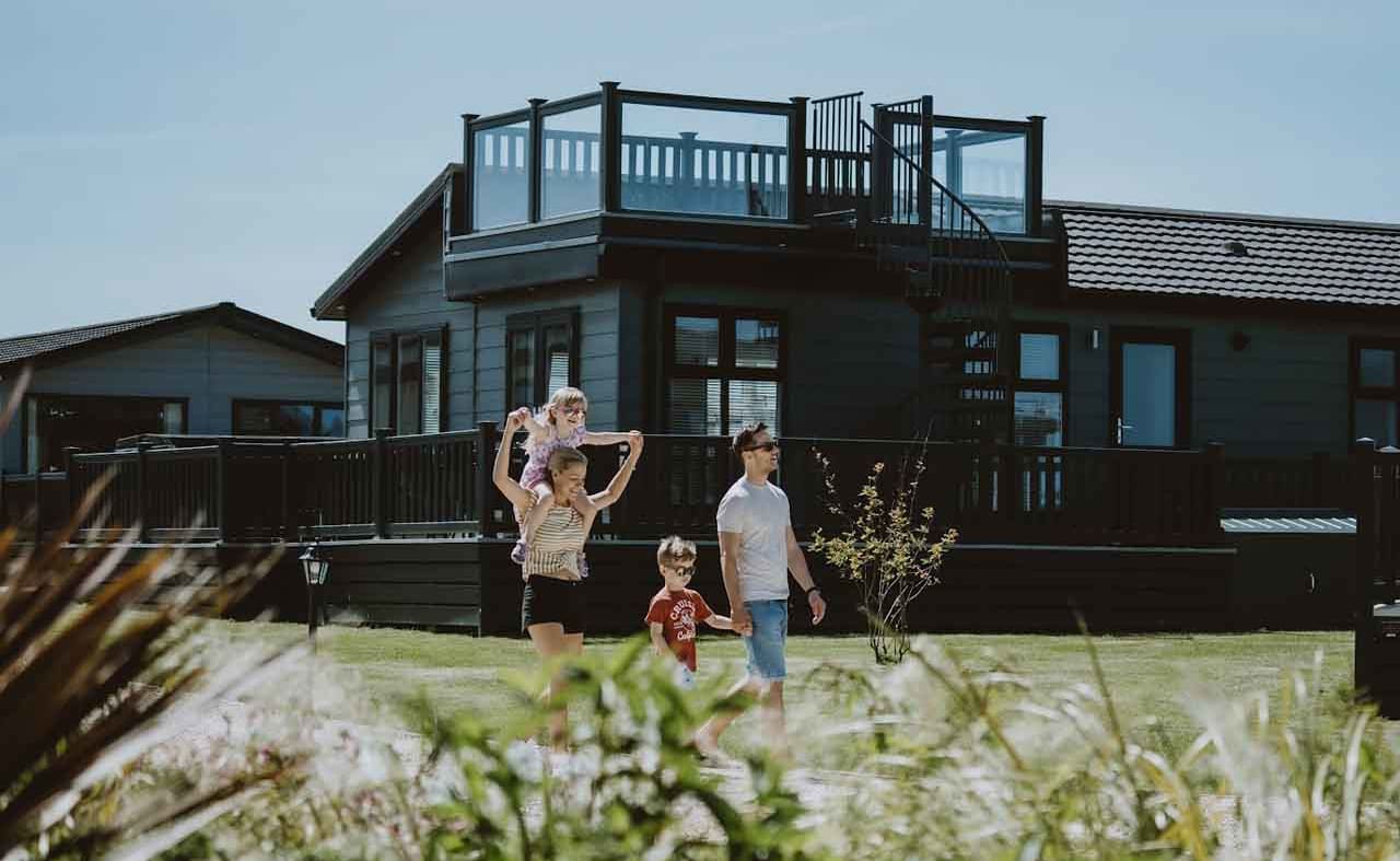 A young family taking a stroll past our stunning holiday homes with roof terraces. One of the two children is on their mum's shoulders. image