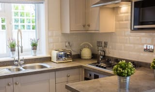 A kitchen area in one of our cottages. Off-white cabinets and grey stone worktops create a clean, welcoming space. Ontop of the worktop is a cream kettle and matching toaster. image