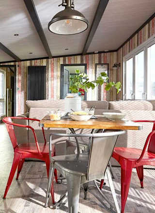 An image of the interior of one of our holiday lodges. There's wooden panneling, a cream fabric sofa and red metal dining chairs around a wooden table.
