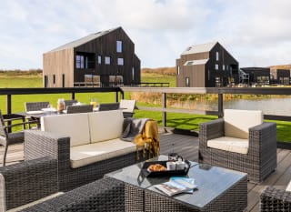 An outside area of one of our luxury barns with outside furniture. Over the balcony are two further lodges. image