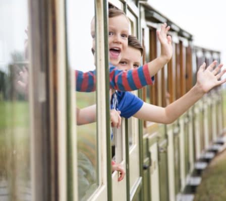 Two children waving at the camera out the window of a train. image