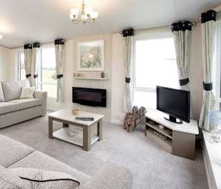 The interior of one of our Luxury holiday lodges. There are two large sofas, a TV, and plenty of space around a coffee table.